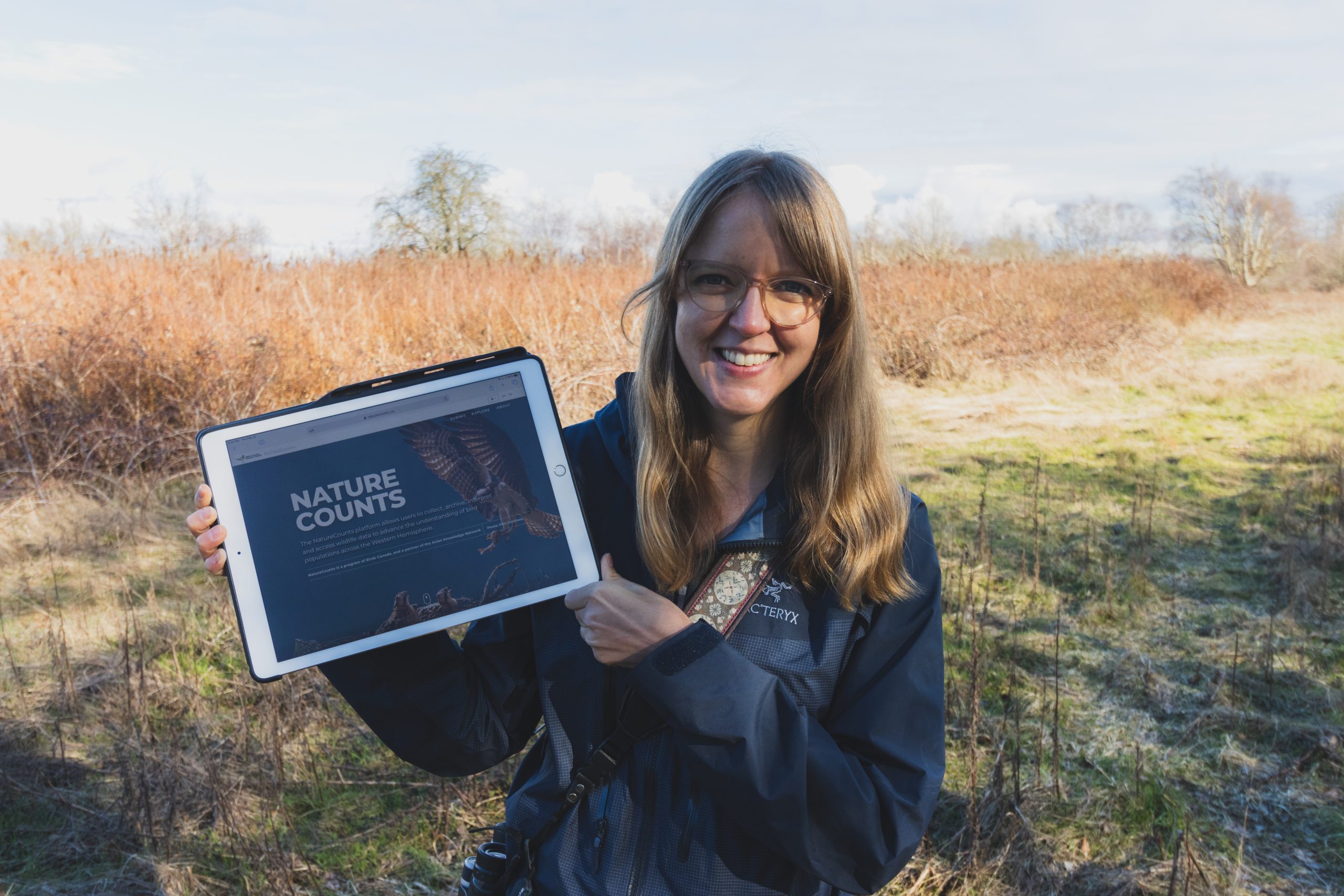 Catherine Jardine, Birds Canada's Associate Director of Data Science and Technology, holds up a tablet displaying NatureCounts out in the field.